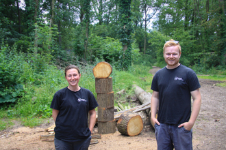 Laura, left, and Alex, right standing in the woods next to a coppiced log