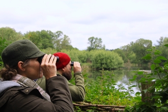 Two people looking through binoculars by a lake