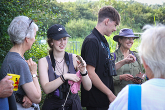 A group of people gathered around a bird ringing demonstration