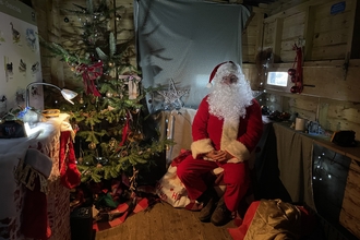 Father Christmas sitting in a grotto decorated with a christmas tree 