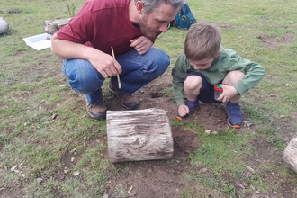 an adult and a child look under a log for minibeasts