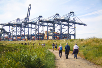 A group of people walking down a gravel track with cranes in the distance