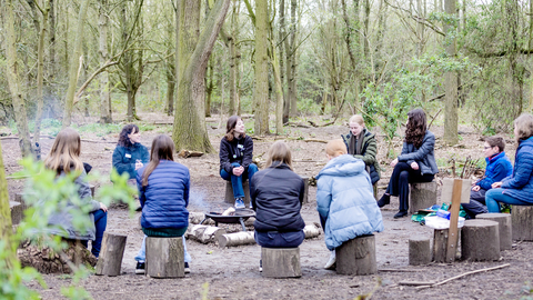 Youth Board members sitting in log circle in woodland, having a meeting