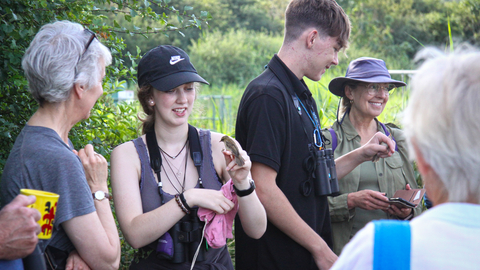 A group of people gathered around a bird ringing demonstration