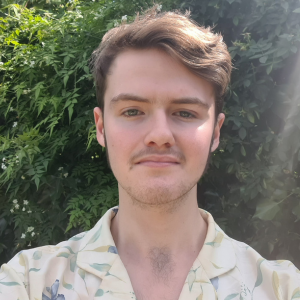 Rowan, Youth Board member, standing infront of a green hedge, image credit Rowan