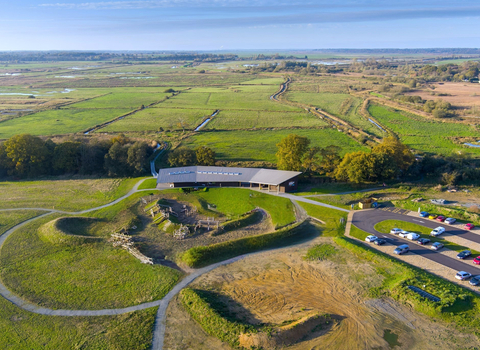 A contemporary visitor centre building sits within the vast green landscape of marshes and wildlife habitat.