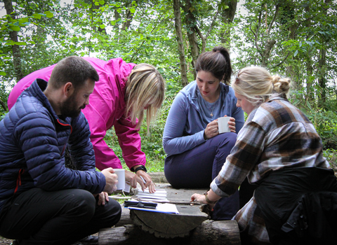 Four people huddle around a log in an ancient woodland analysing bark types.