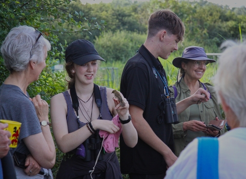 A group of people gathered around a bird ringing demonstration